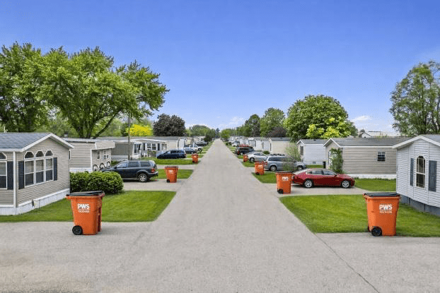 View of a mobile home park street lined with trailers and trees under a clear sky.